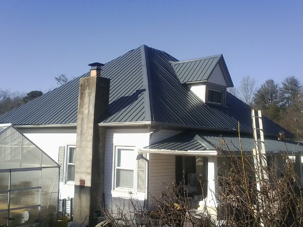 Dark blue standing seam metal roof on a white farmhouse with dormer — Slate & Tile Roof Repair by Roofing Brothers in Goldston