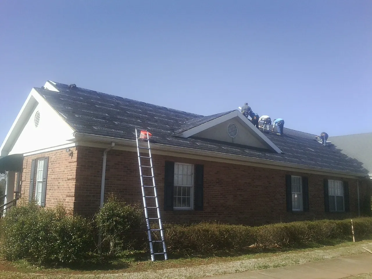 Crew tearing shingles off a brick ranch roof with a ladder set — Emergency Roof Repair work by our crew in Goldston