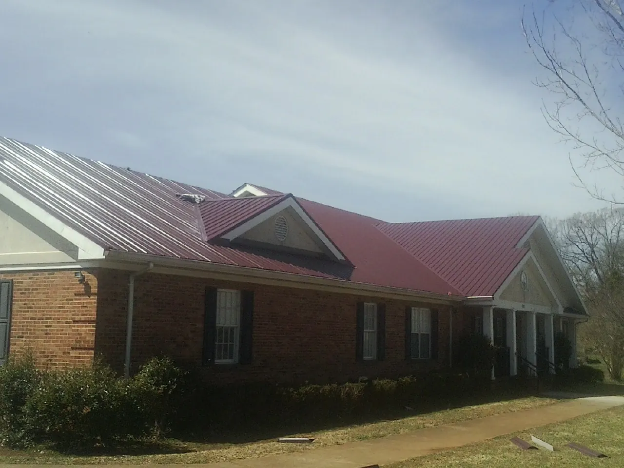 Red metal roof with gabled entries on a long brick building, from a Hail Damage Roof Repair job in Goldston