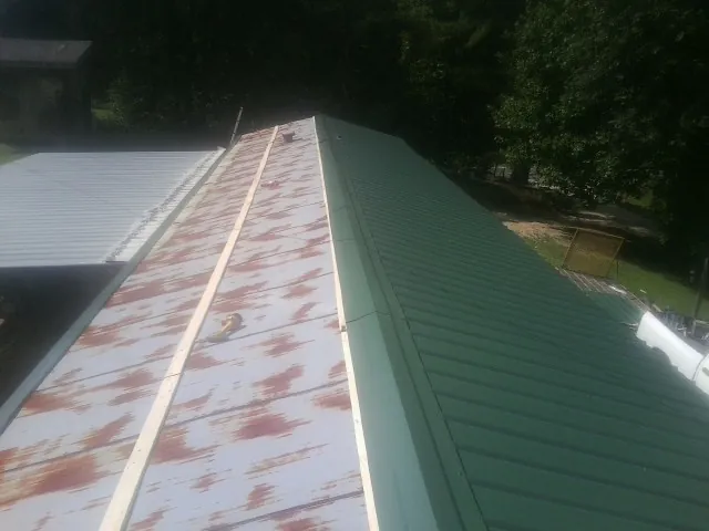 Old rusted panels beside newly installed green metal roofing — Wind Damage Roof Repair by Roofing Brothers in Goldston