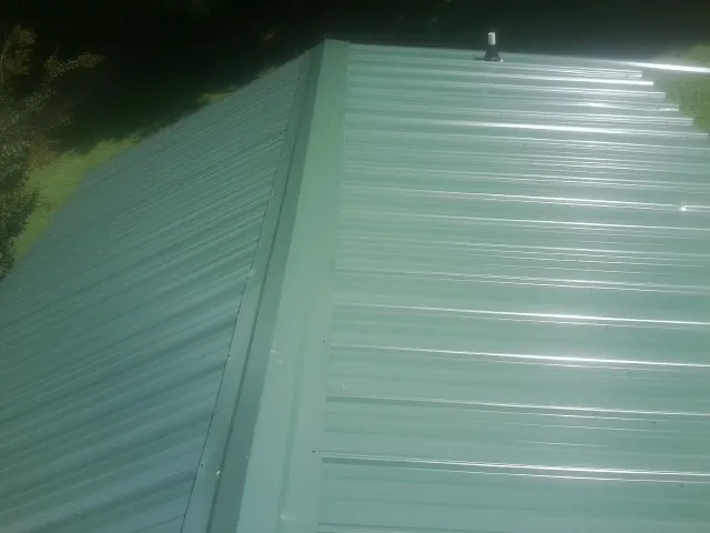 New green metal panels meeting at the ridge of a roof — Flat Roof Repair work by our crew in Goldston