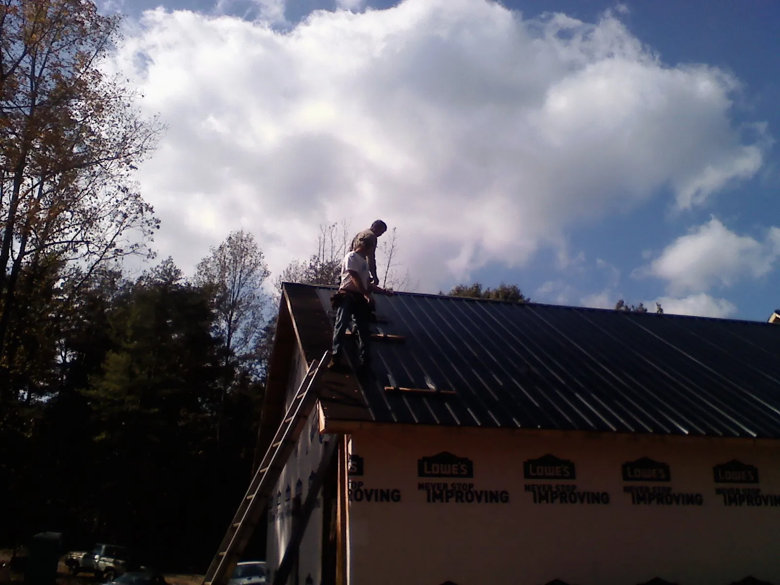 Roofer fastening dark metal panels high against a cloudy sky, from a Roof Inspection job in Goldston