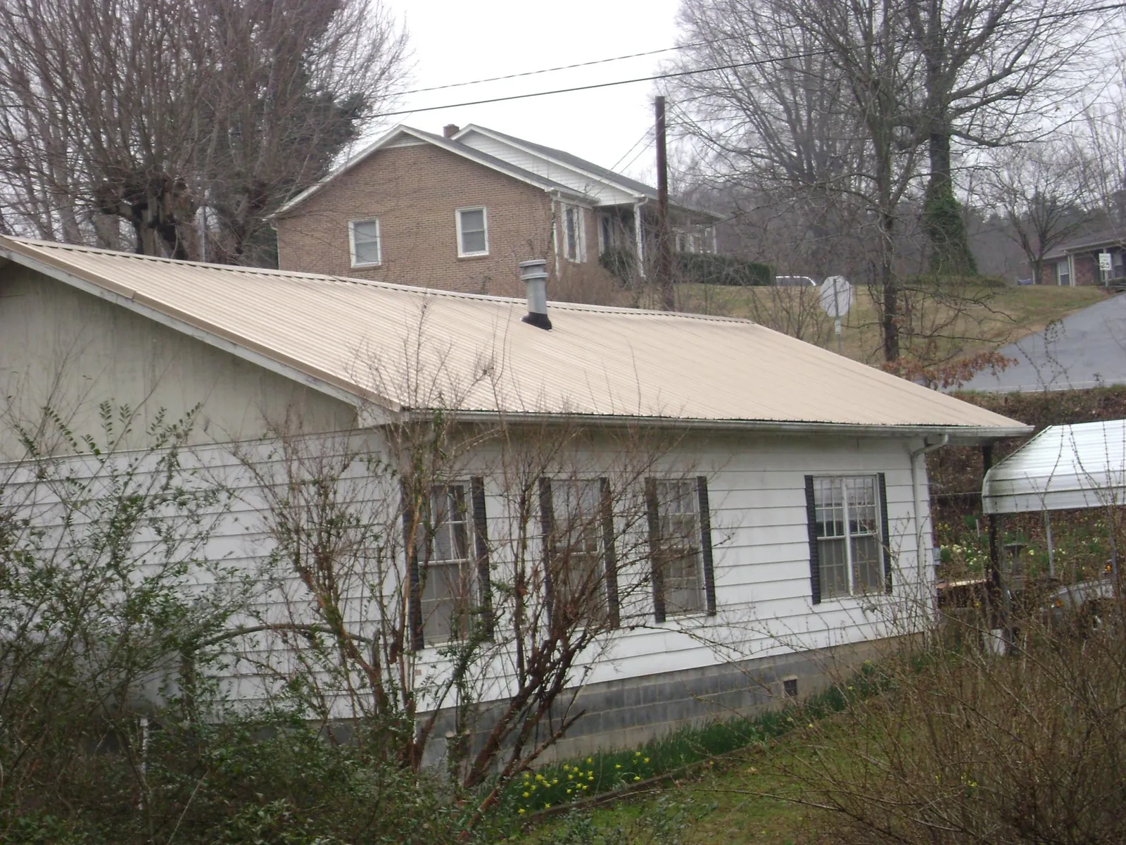 Tan metal roof on a white sided house set into a hillside — Commercial Roofing by Roofing Brothers in Goldston