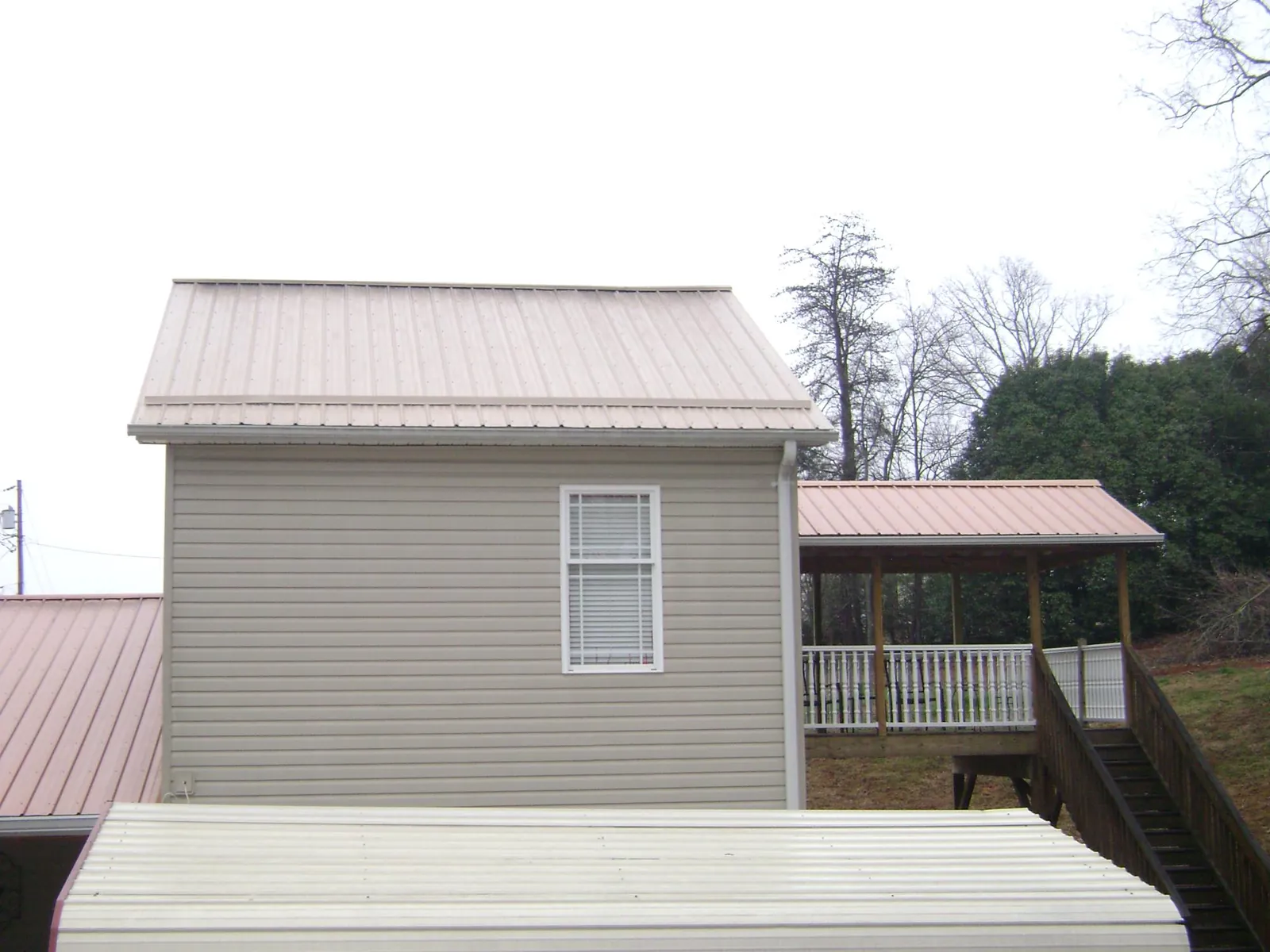 Tan metal roofs on a two story addition and attached porch, from a Roof Replacement job in Goldston